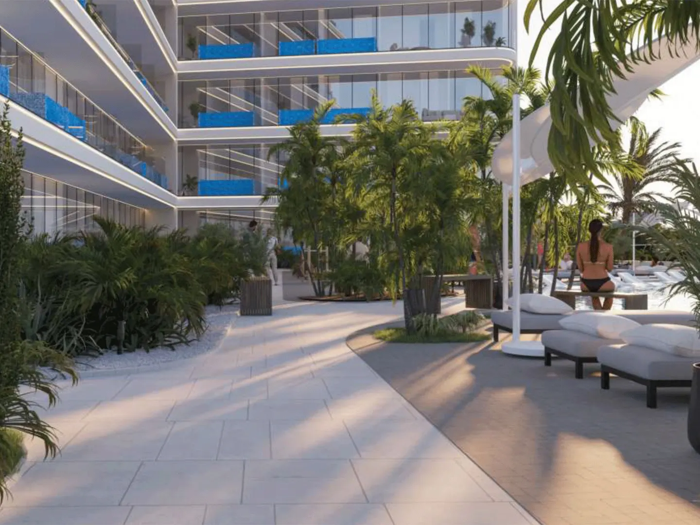 Exterior view of a modern white building with blue balconies, lush greenery, and a pool area with lounge chairs and a woman sitting on a bench.