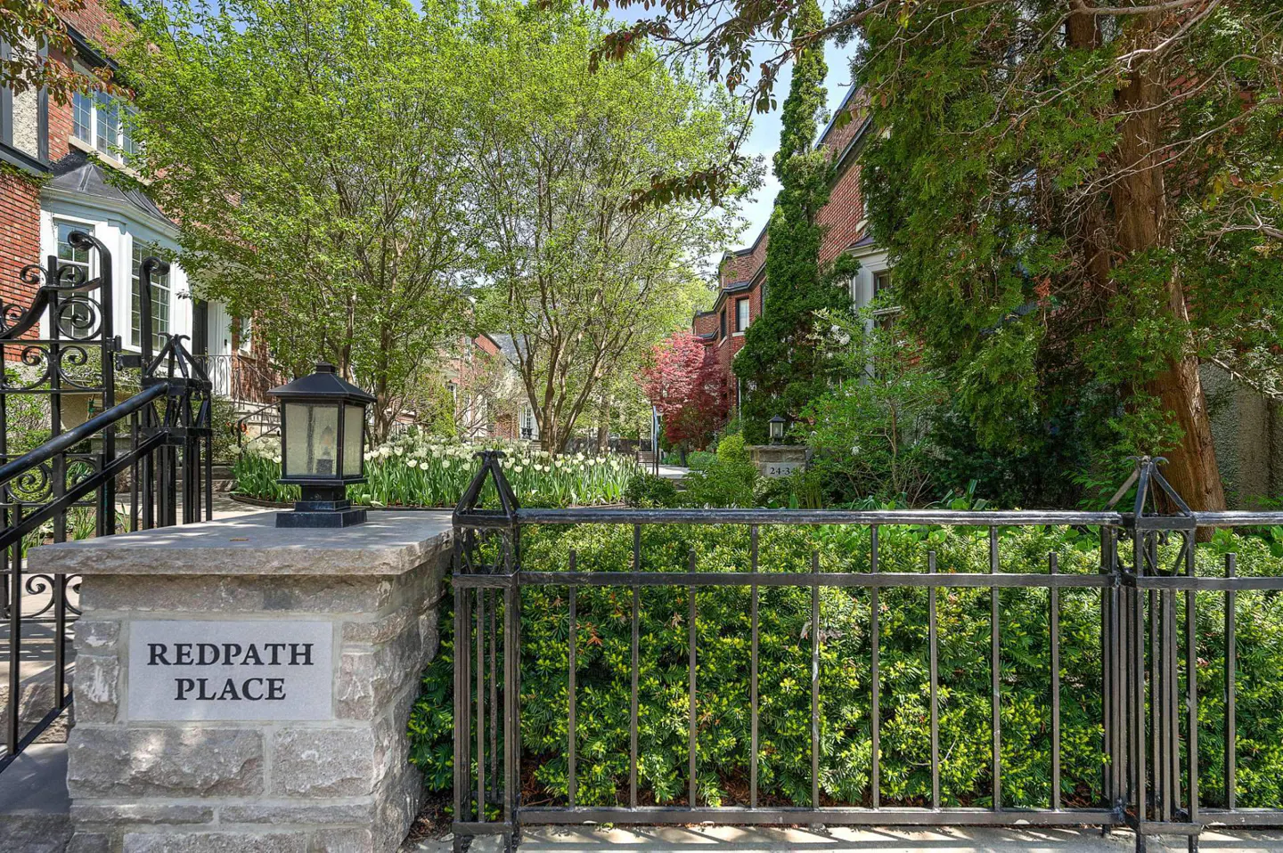 "Redpath Place" stone sign with black iron fence and lantern. Lush green trees and brick houses line the street.