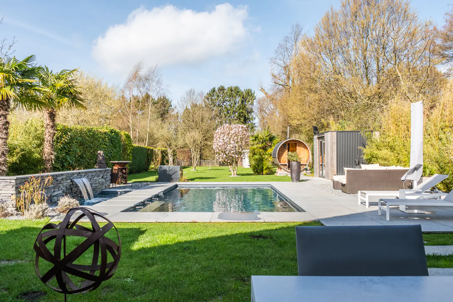 A backyard with a pool, sauna, lounge chairs, and green grass on a sunny day.