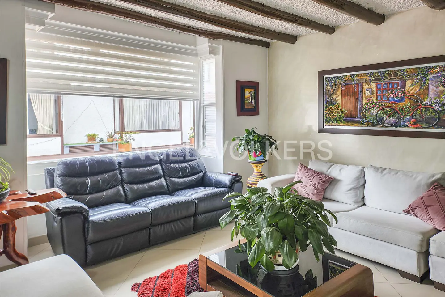 Living room with a black leather sofa, white sofa with pink pillows, and a painting of a bicycle.