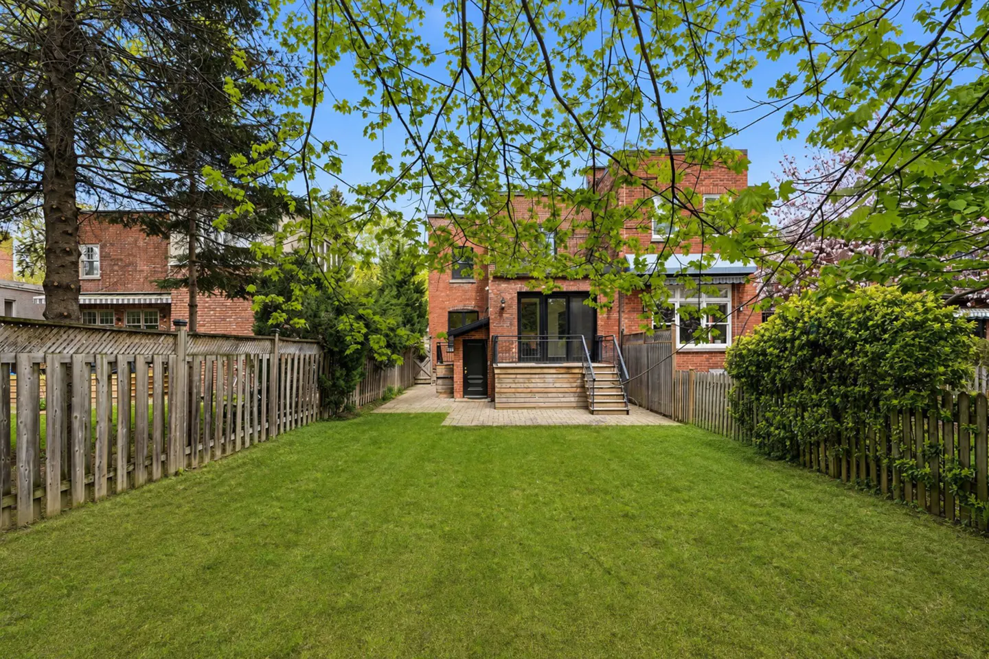 A backyard with a green lawn, a brick house, and a wooden fence.