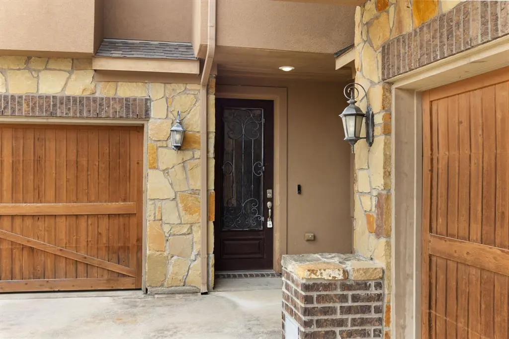 Exterior view of a home with stone and tan stucco, featuring a dark wood door with ironwork, and wooden garage doors.