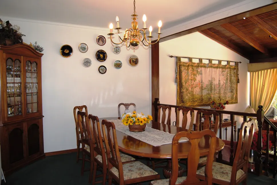 Dining room with a wood table, eight chairs, and a gold chandelier. A china cabinet and decorative plates are on the wall.