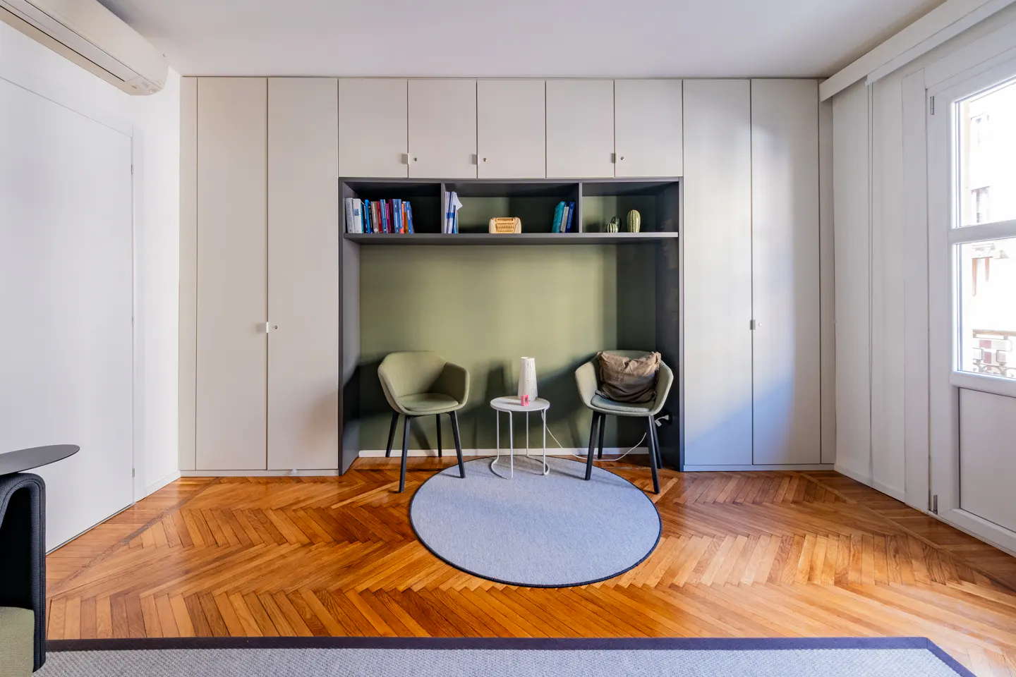 Interior view of a room with parquet floors, built-in shelves, two chairs, and a round rug.