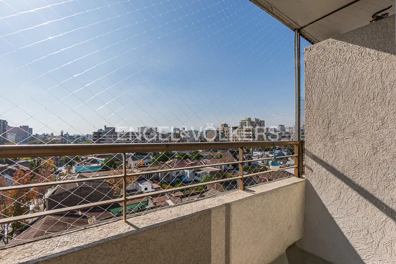 Balcony view with safety net, metal railing, and cityscape. Beige wall on the right, blue sky above.