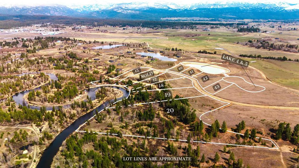 Aerial view of real estate lots with approximate lot lines, a winding river, trees, lakes, and snow-capped mountains in the background.