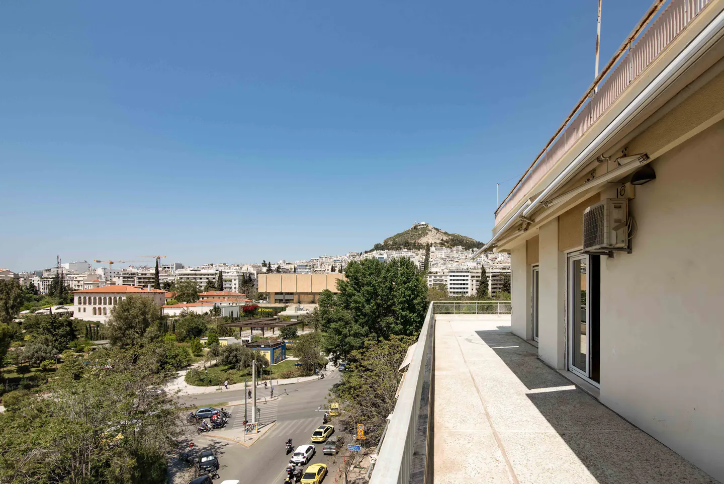 View from a balcony overlooking Athens, Greece, with Mount Lycabettus in the background on a sunny day.