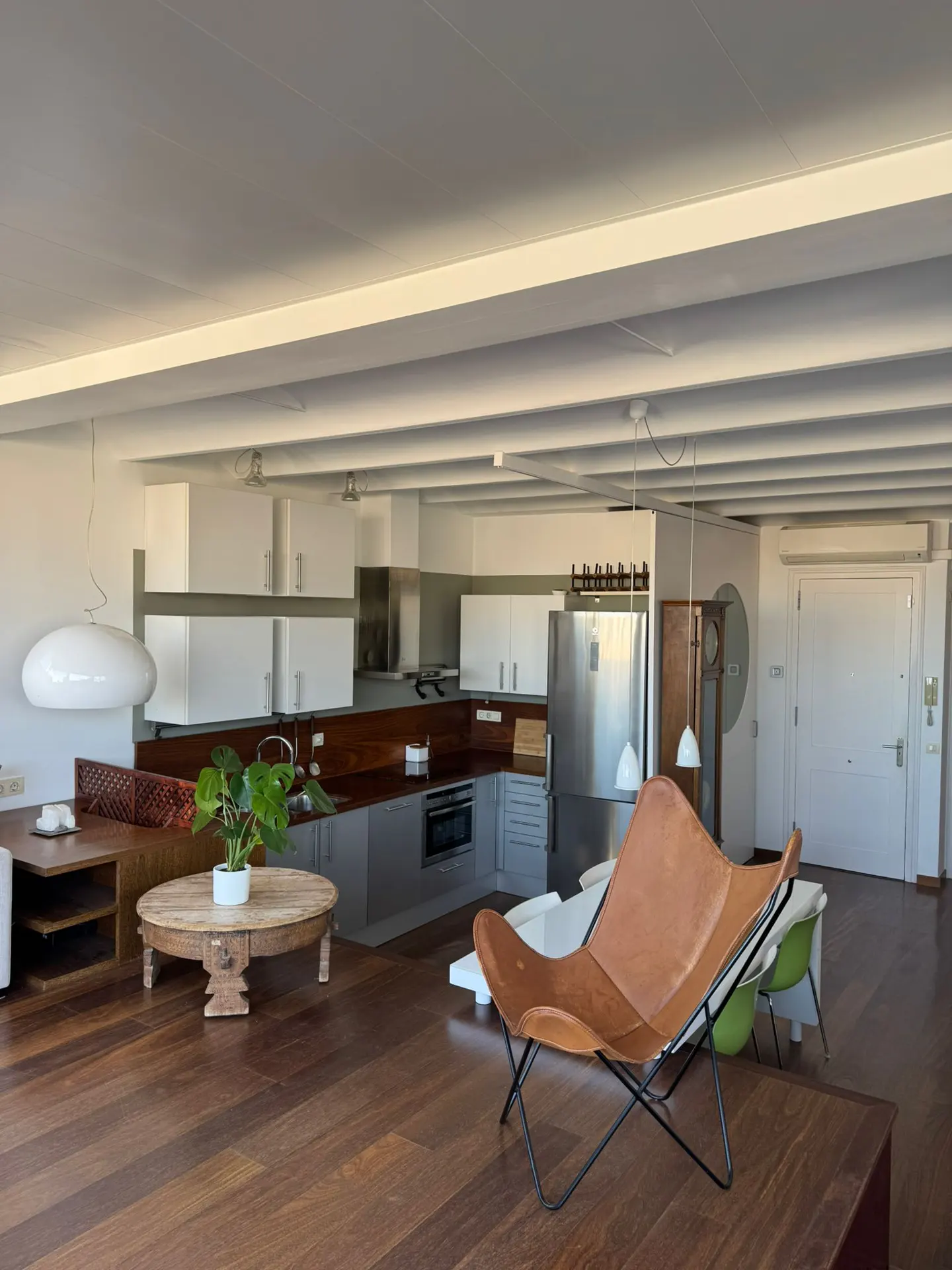 Open-concept living space with wood floors, white cabinets, and a brown leather butterfly chair.