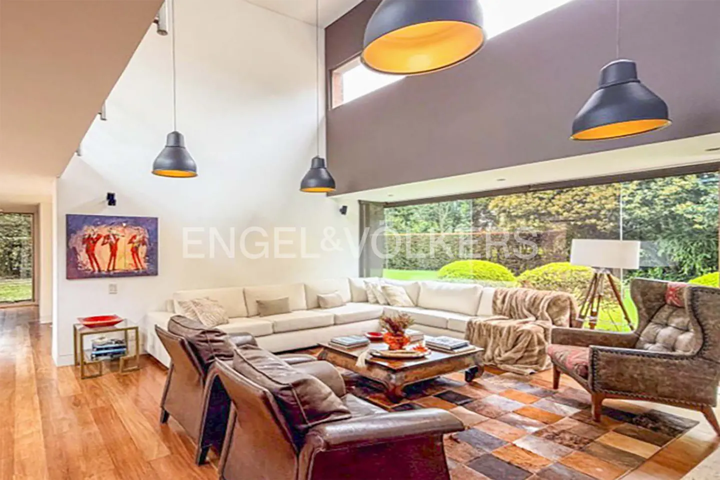 Bright living room with white sectional sofa, brown leather chairs, and a large window overlooking a green garden.