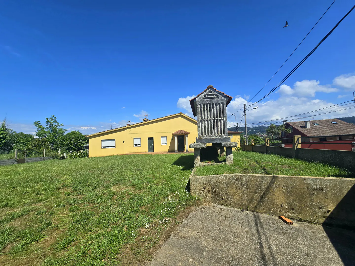 A yellow house with a traditional granary on a green lawn under a blue sky.