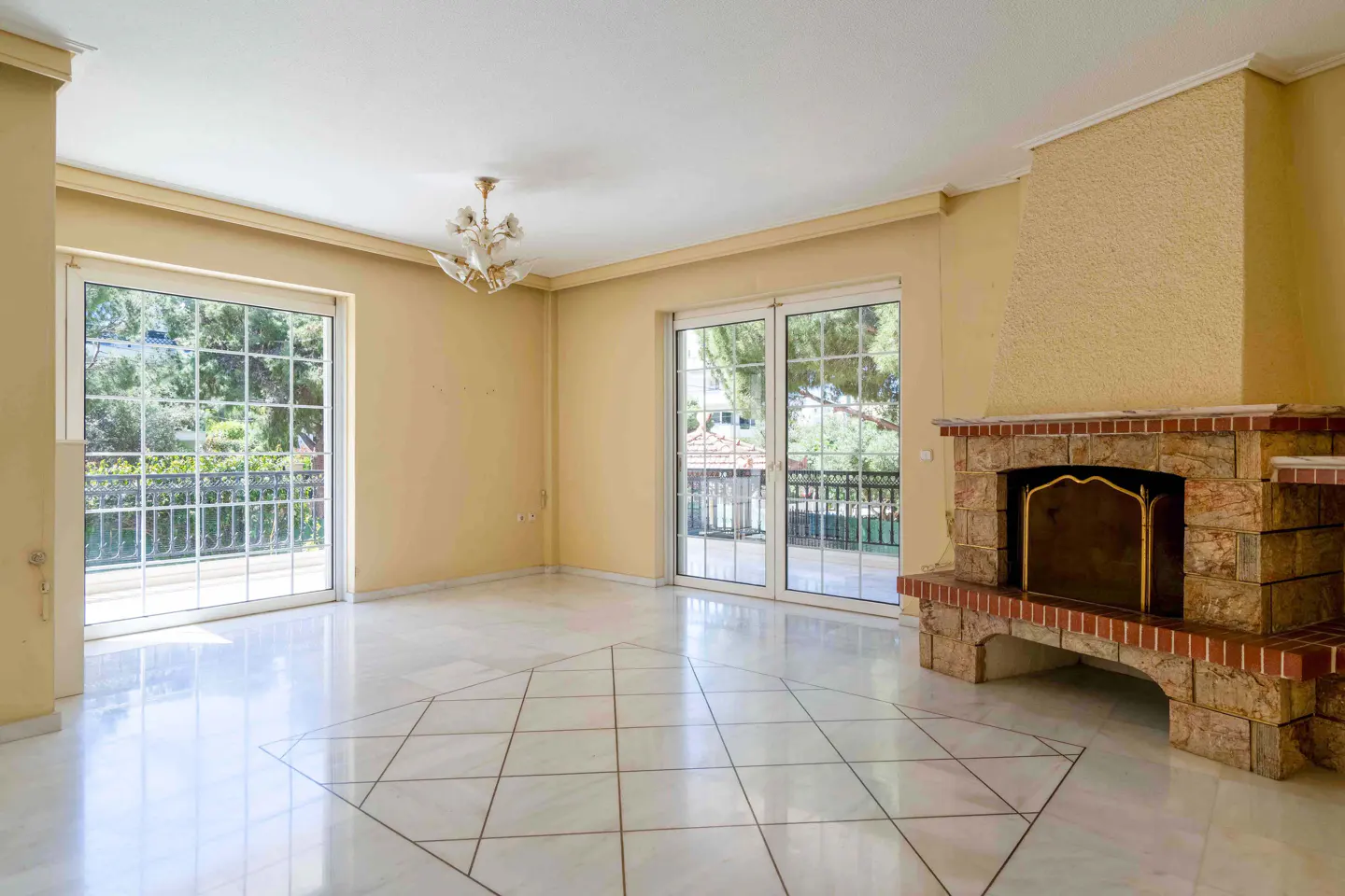 Bright, empty living room with marble floors, stone fireplace, and sliding glass doors to a balcony. Walls are light yellow.