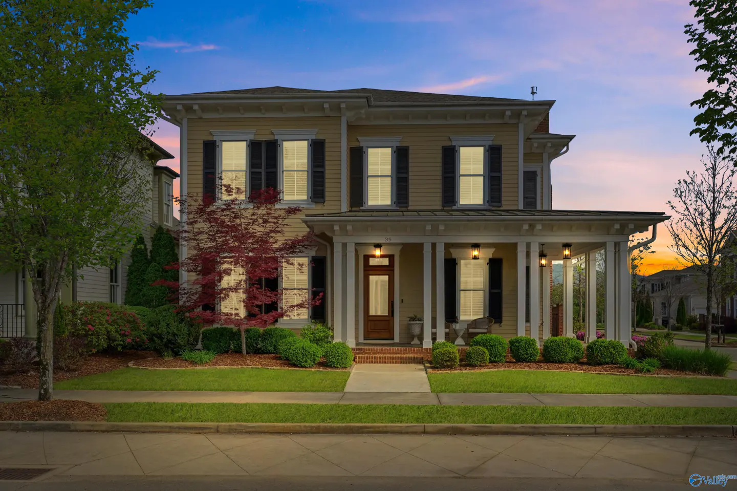Two-story tan house with black shutters and a covered porch at dusk.
