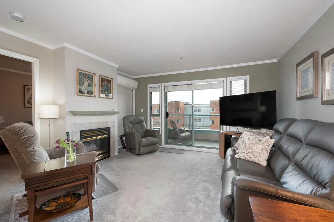 Living room with gray carpet, leather sofa, recliner, fireplace, and balcony with a view of buildings.