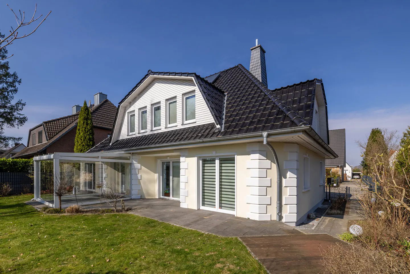 A cream-colored house with a black roof, white trim, and a glass-enclosed patio on a sunny day.