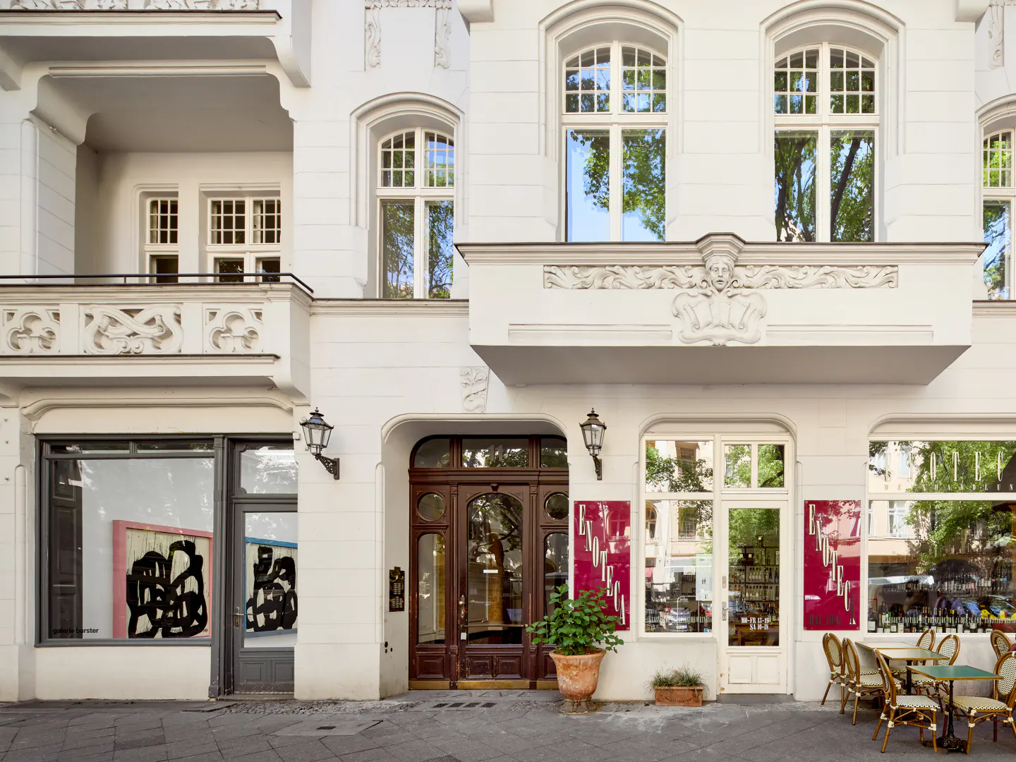 Exterior of a white building with a gallery, restaurant, and apartments. The restaurant has outdoor seating.