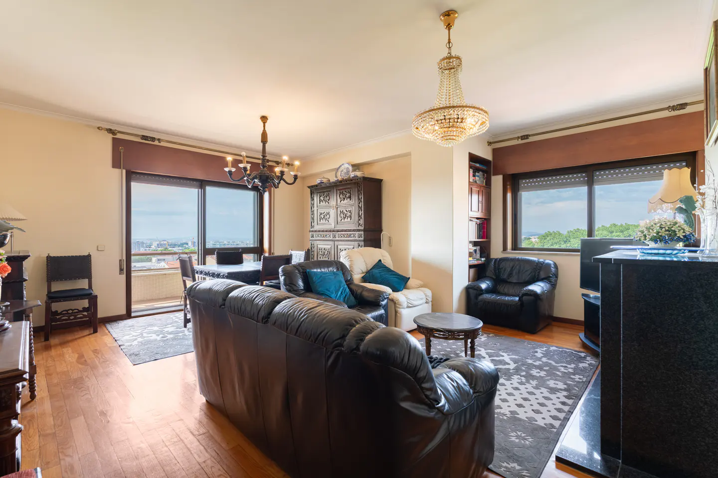 A living room with hardwood floors, a black leather sofa, a dining table, and a balcony with a city view.