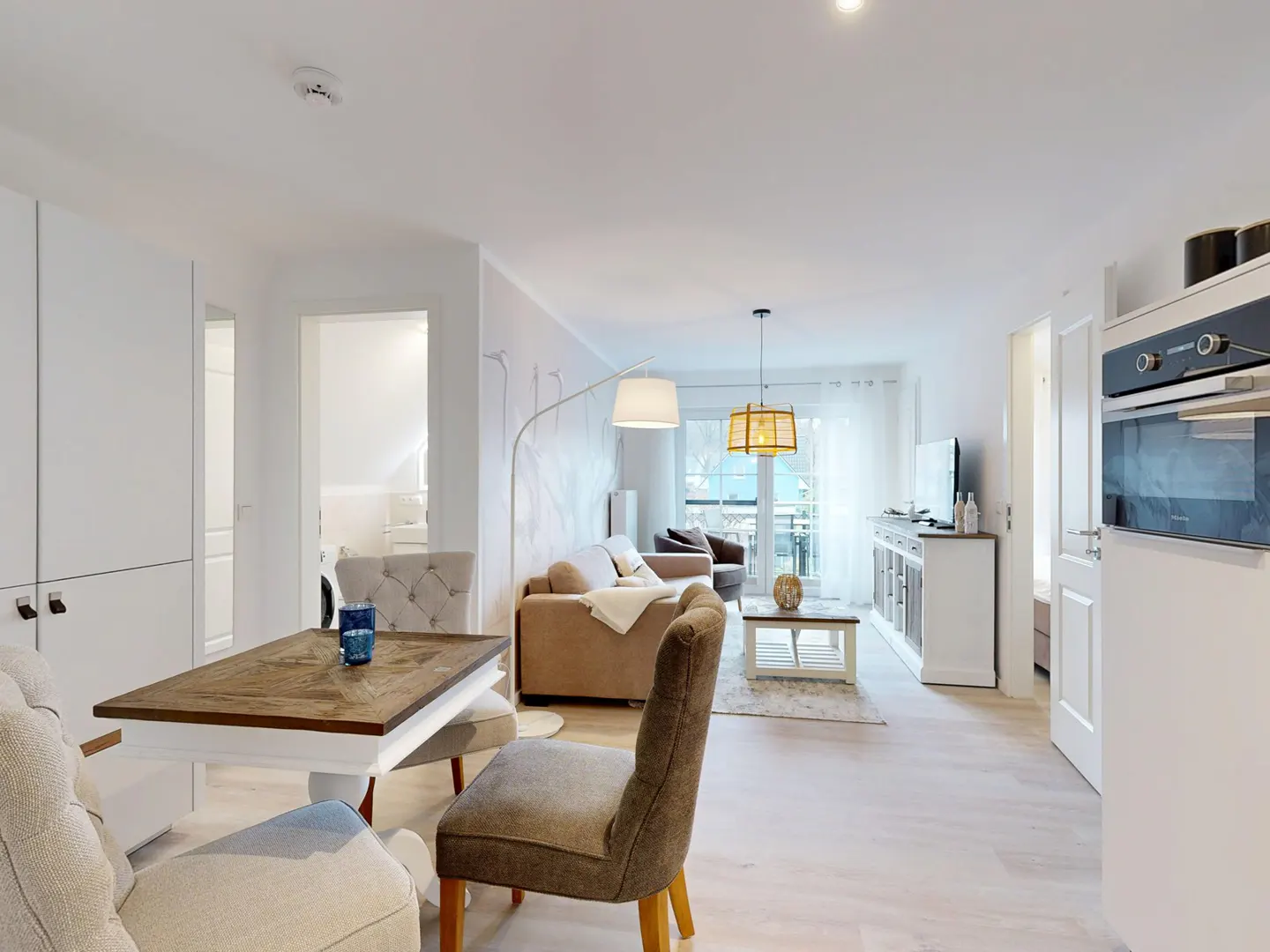 Bright, open-plan living space with a dining table, sofa, and kitchen area. Neutral tones and natural light create a welcoming atmosphere.
