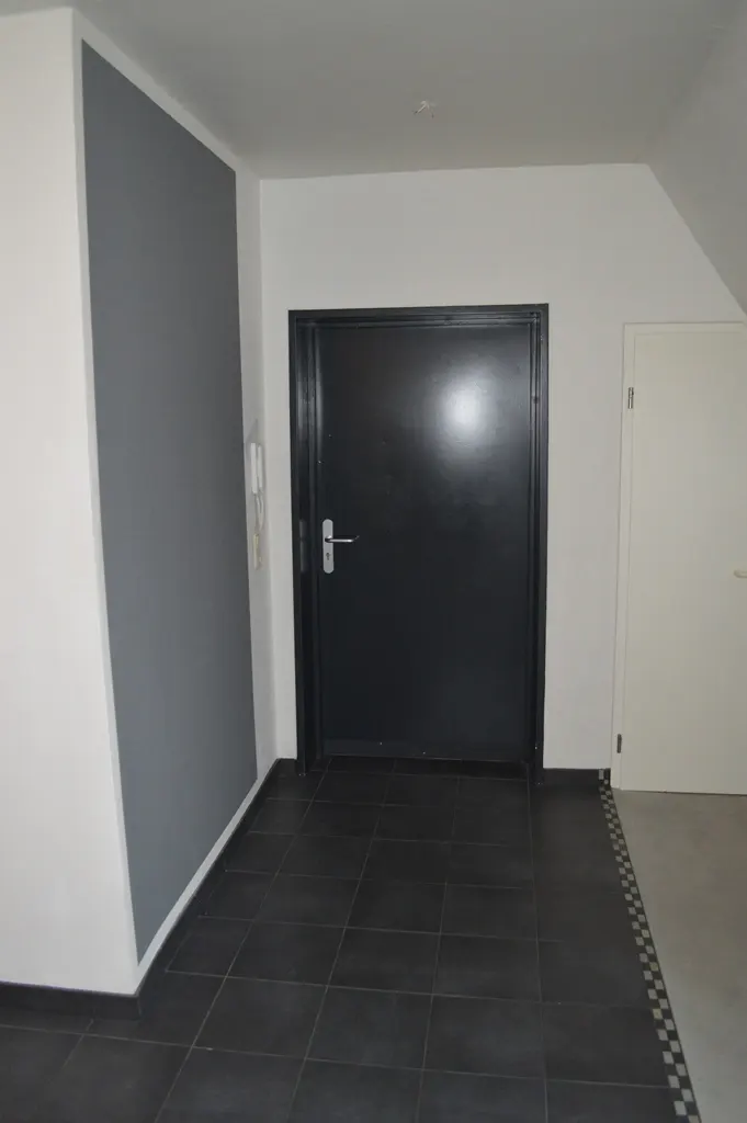 Interior view of a hallway with black tile flooring, a black door, and a white door. The walls are white with a gray accent wall.