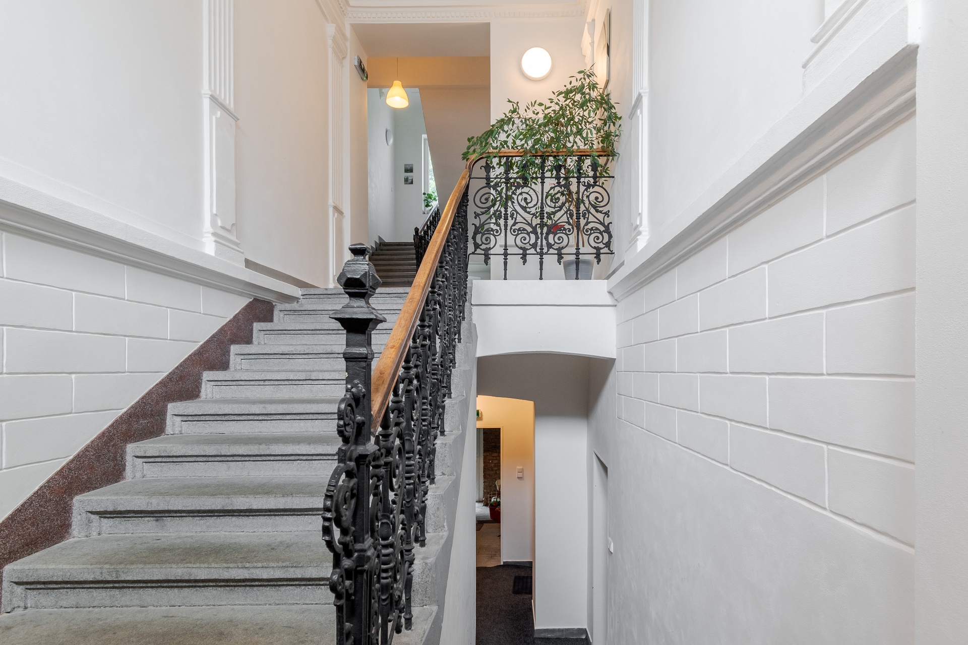Bright white staircase with stone steps, ornate black iron railing, and a potted plant on the landing.