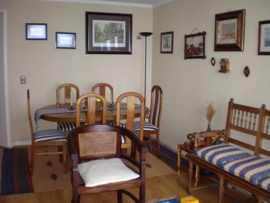 A dining room with a wooden table and chairs, a bench with blue and white striped cushions, and framed artwork on the walls.