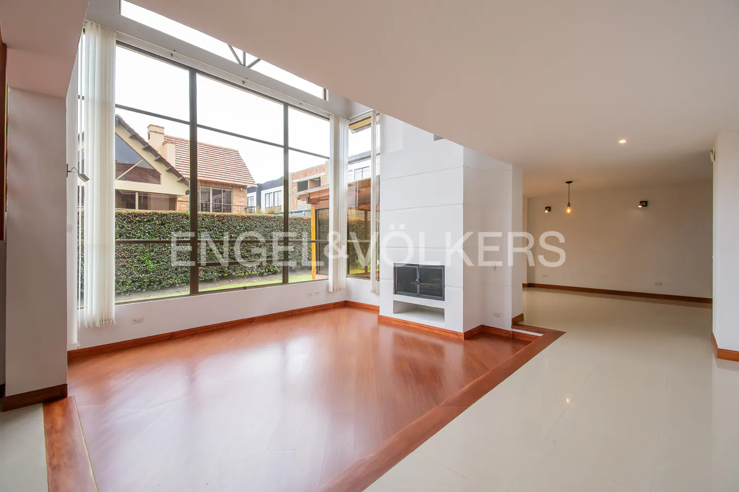 Spacious living room with hardwood floors, a modern fireplace, and floor-to-ceiling windows overlooking a garden.
