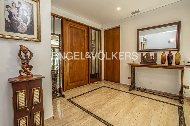 Real estate foyer with marble floors, wooden doors, and a console table with decorative vases. A framed picture hangs on the wall.