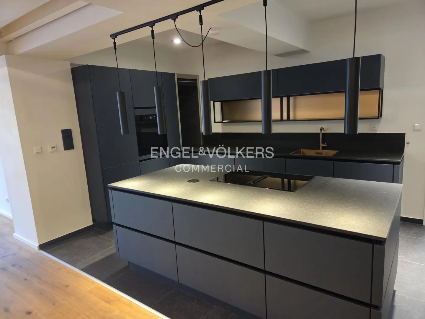 Modern kitchen with gray cabinets, island, and black countertops. Pendant lights hang above the island.
