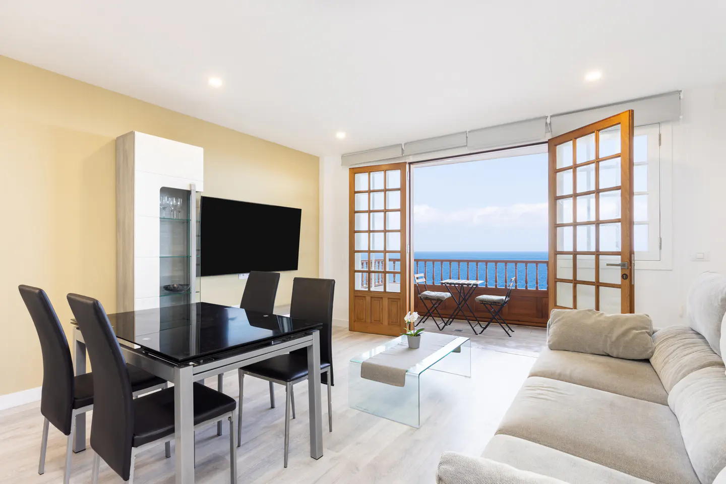 Bright living room with a black dining table, beige sofa, and balcony with ocean view.