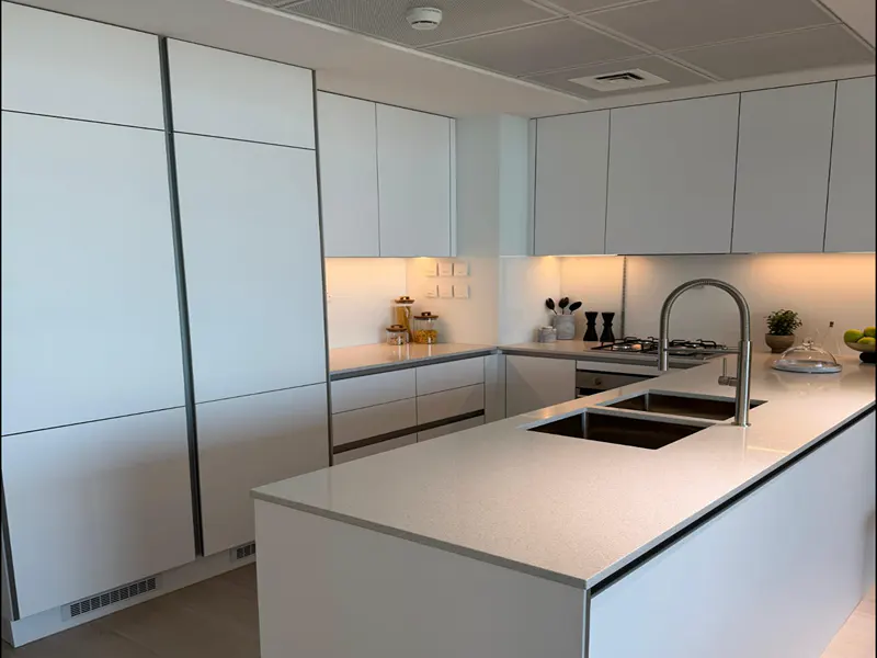 A modern kitchen with white cabinets, a large island with a sink and faucet, and under-cabinet lighting.