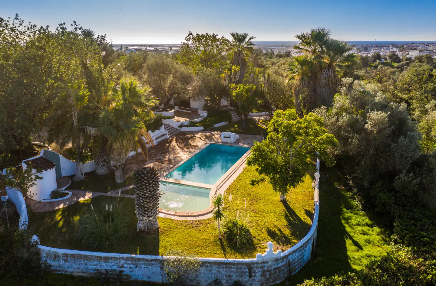 Aerial view of a turquoise pool surrounded by green trees and a white stone wall.