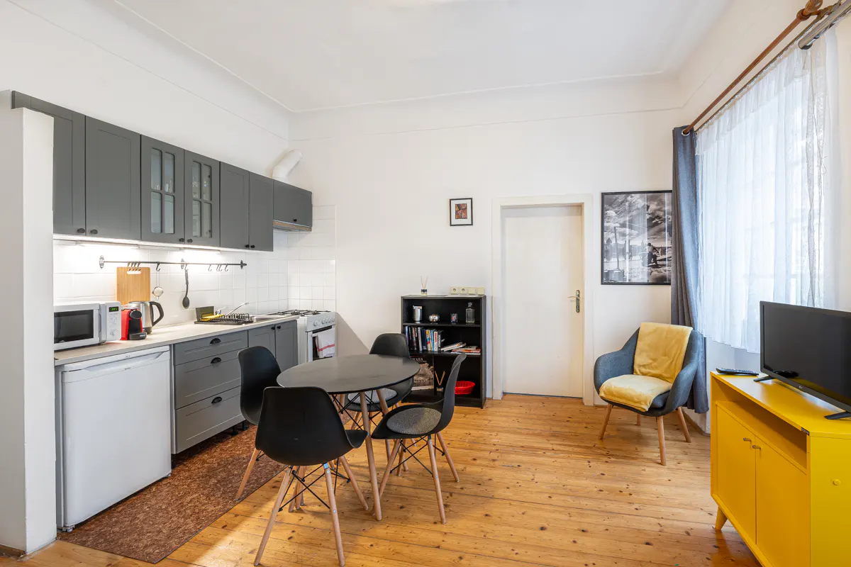 Bright apartment interior with wood floors, gray kitchen cabinets, a black dining table, and a yellow TV stand.
