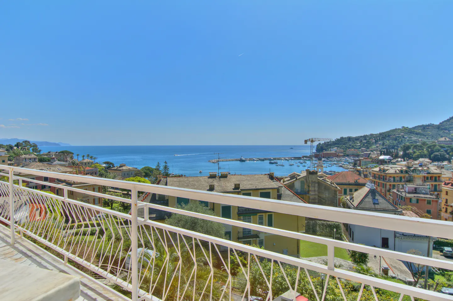 View from a white balcony overlooking a harbor with boats, buildings, and a blue sky.