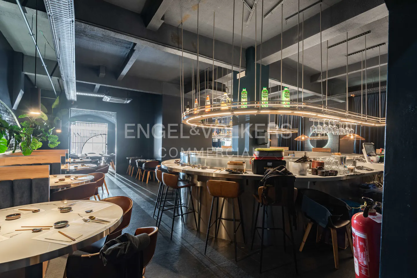Interior view of a modern restaurant with a circular bar, tables set for dining, and industrial-style lighting.