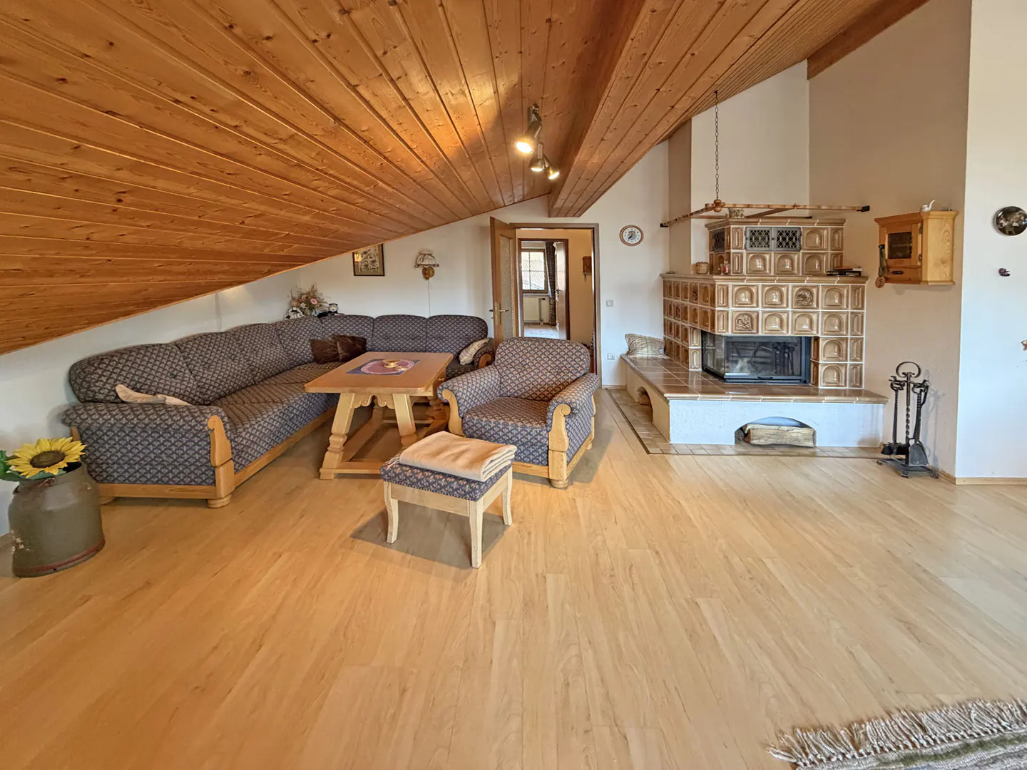 Living room with wood floors, wood ceiling, patterned sofa and chair, and a large tiled fireplace.