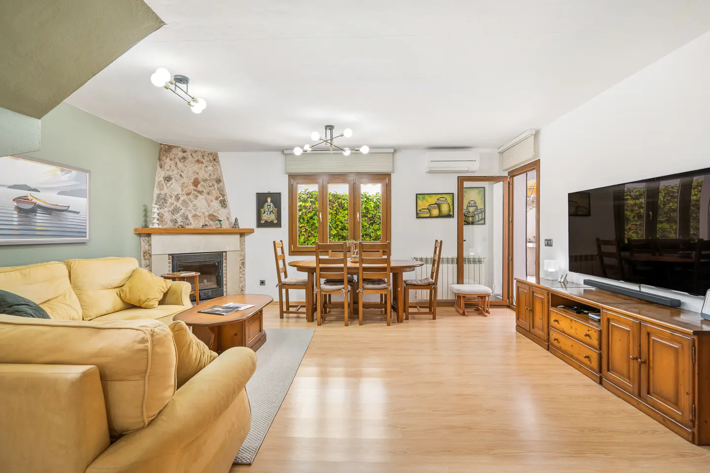 A living room with a yellow sofa, wooden table and chairs, fireplace, and a large TV on a wooden cabinet.