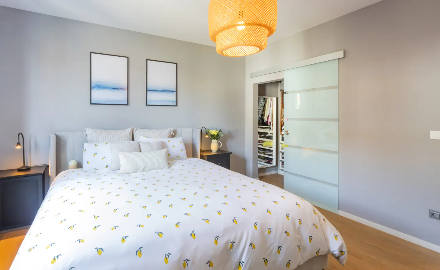 Bedroom with a white bedspread with yellow lemons, gray walls, and a closet with a sliding glass door.