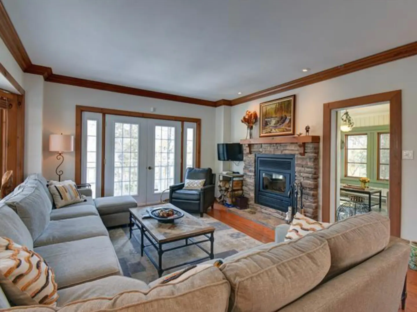 Living room with a stone fireplace, a gray sectional sofa, and a coffee table. French doors lead to the outside.