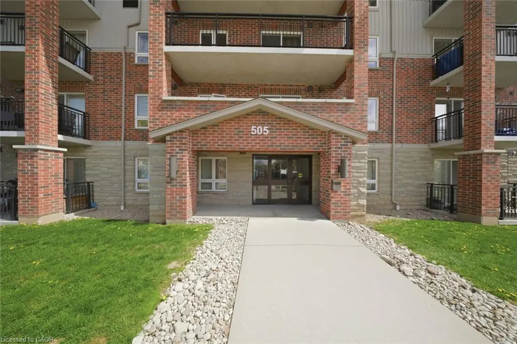 Exterior of a brick apartment building with balconies. The entrance has a small roof and the number 505 above the door. A concrete walkway leads to the entrance.