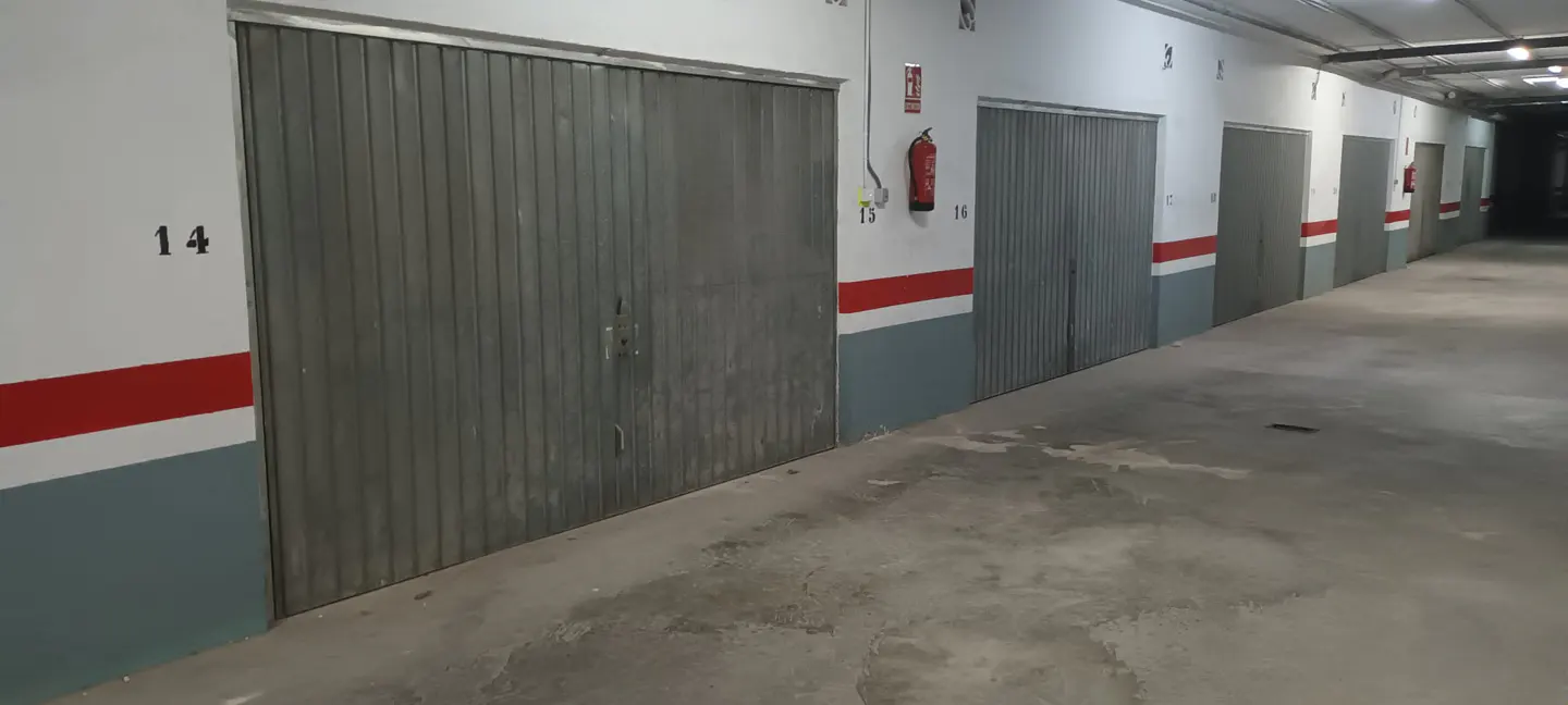 Indoor parking garage with numbered metal storage units, white walls with red and grey stripes, and a red fire extinguisher.