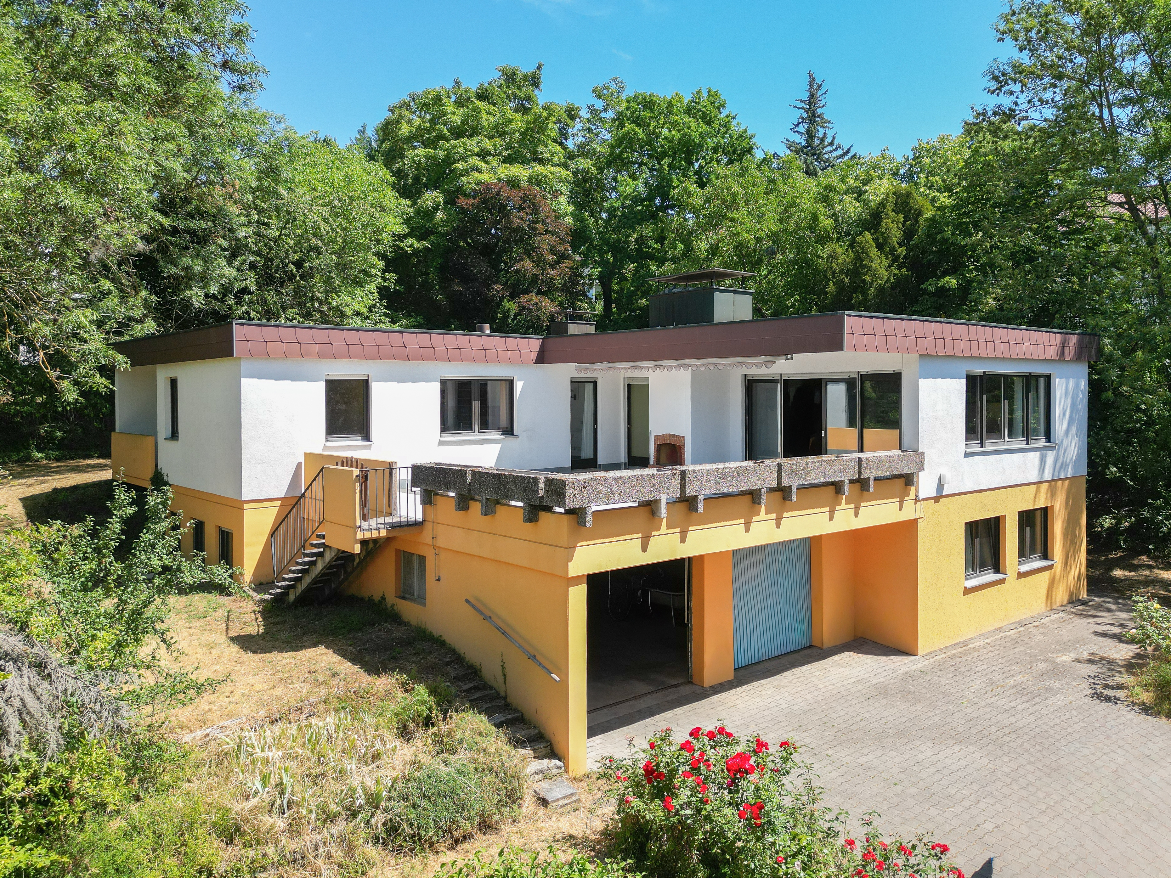 Modern two-story house with white and yellow exterior, a large elevated terrace, and a ground-level garage.
