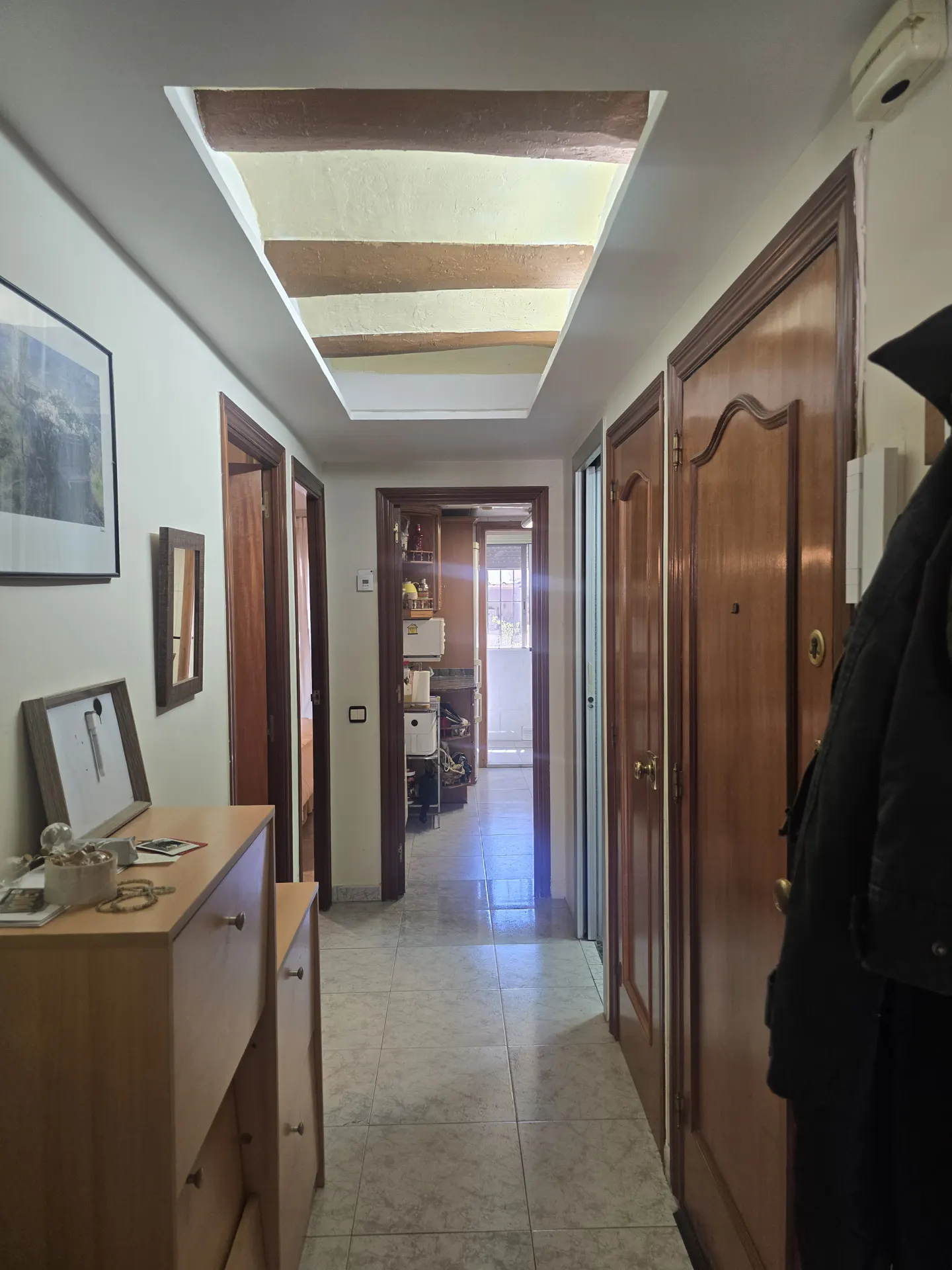 Hallway with tile floor, wooden doors, and a decorative ceiling with beams. A dresser is on the left.