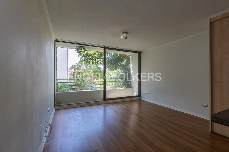 Empty room with wood floors, white walls, and a large window overlooking a balcony with trees.