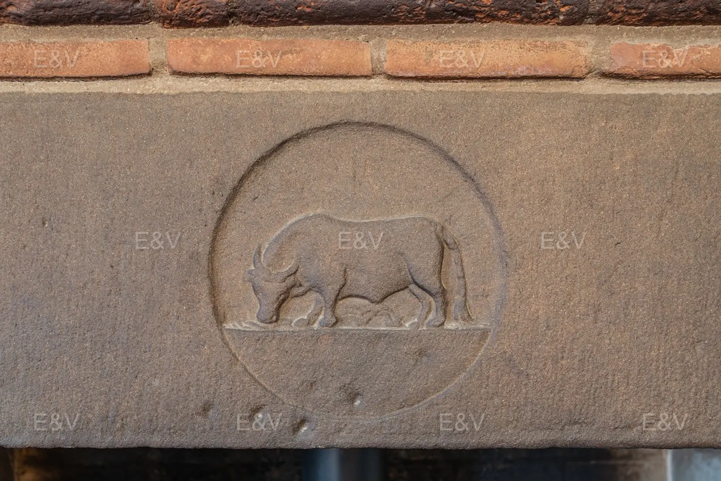 Stone fireplace detail with a carved bull in a circle, under a brick mantel.