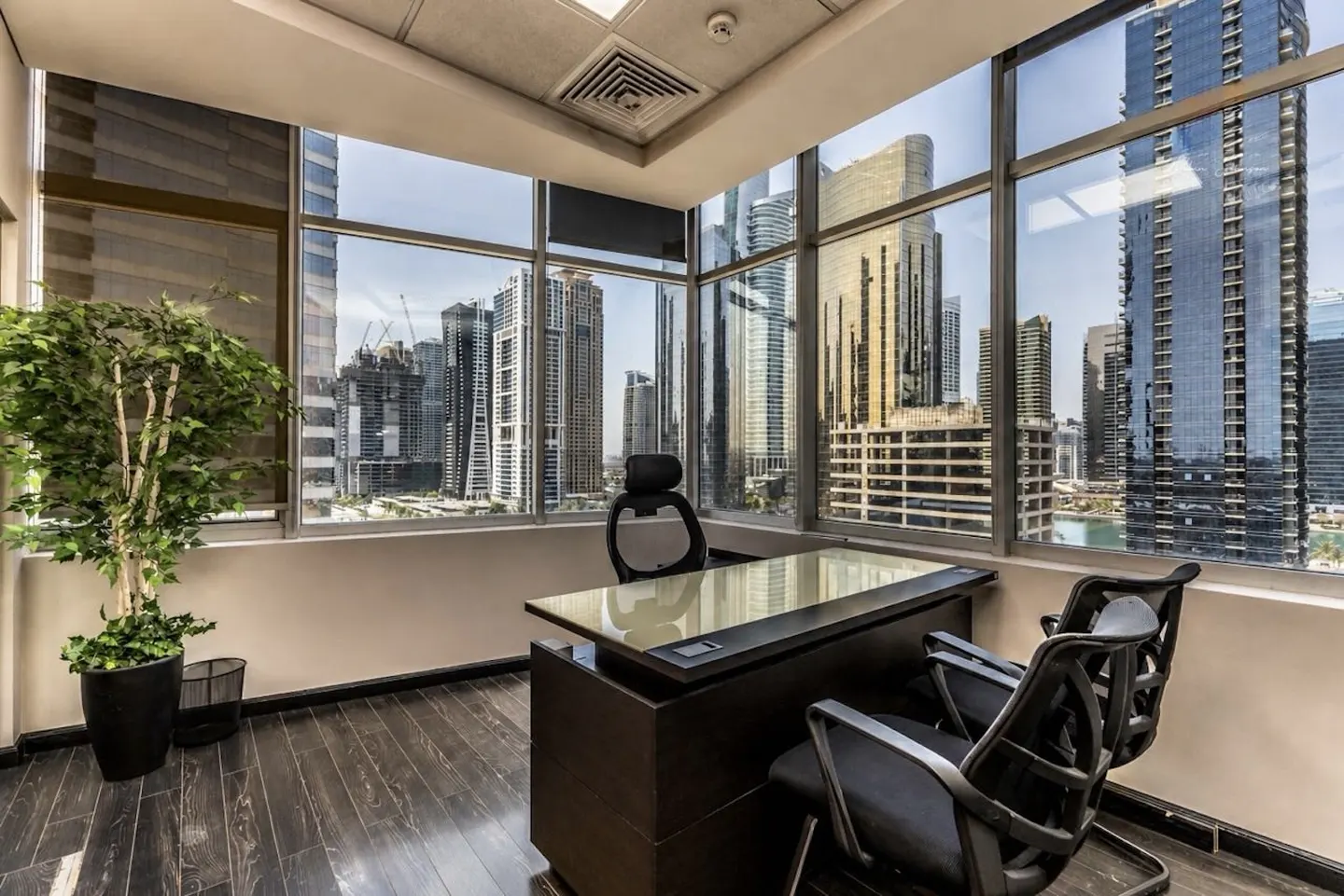 Office interior with a dark wood desk and chairs, a potted plant, and a large window overlooking a cityscape.