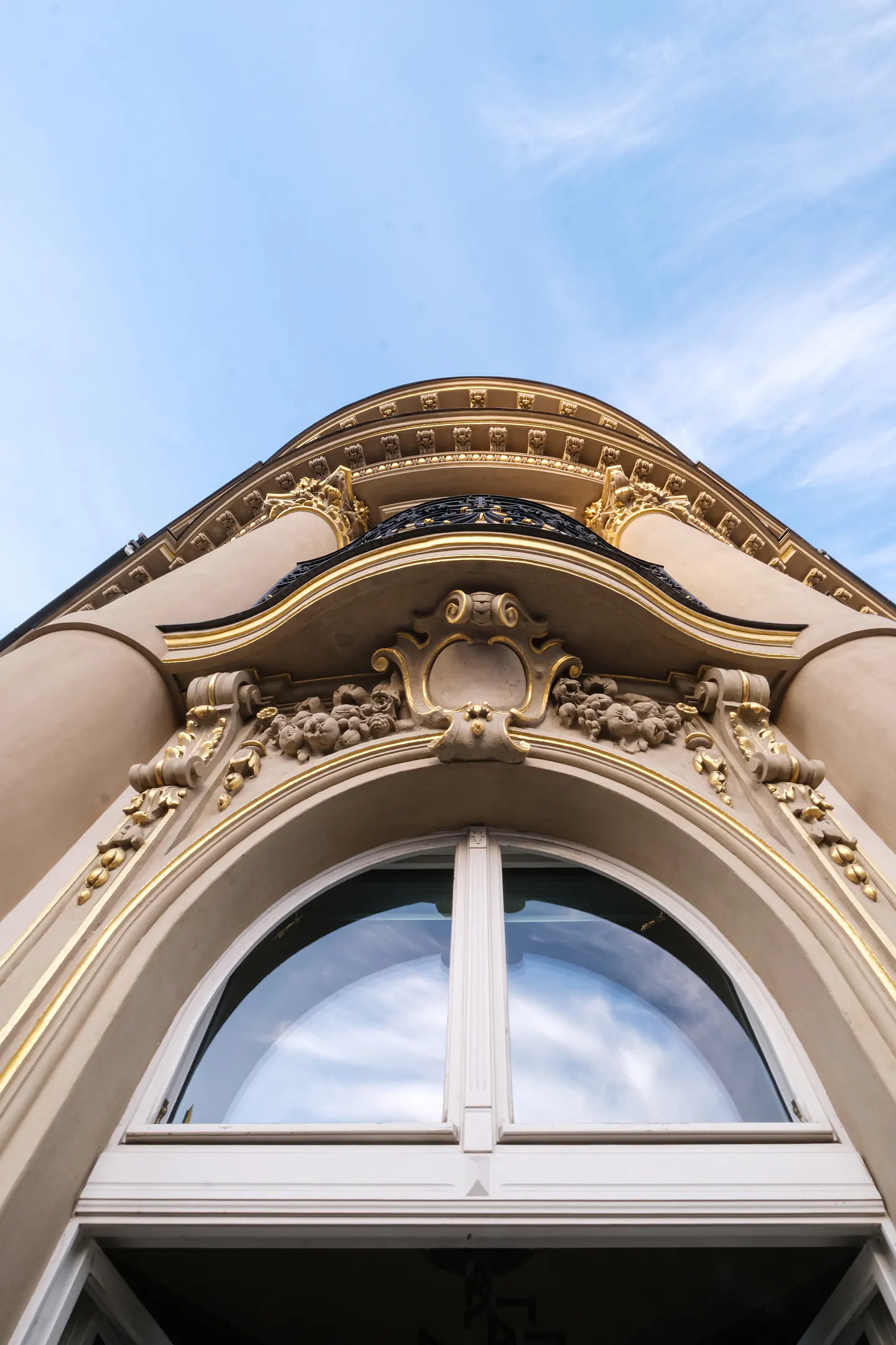Low angle view of a building's arched window with gold trim and decorative molding against a blue sky.
