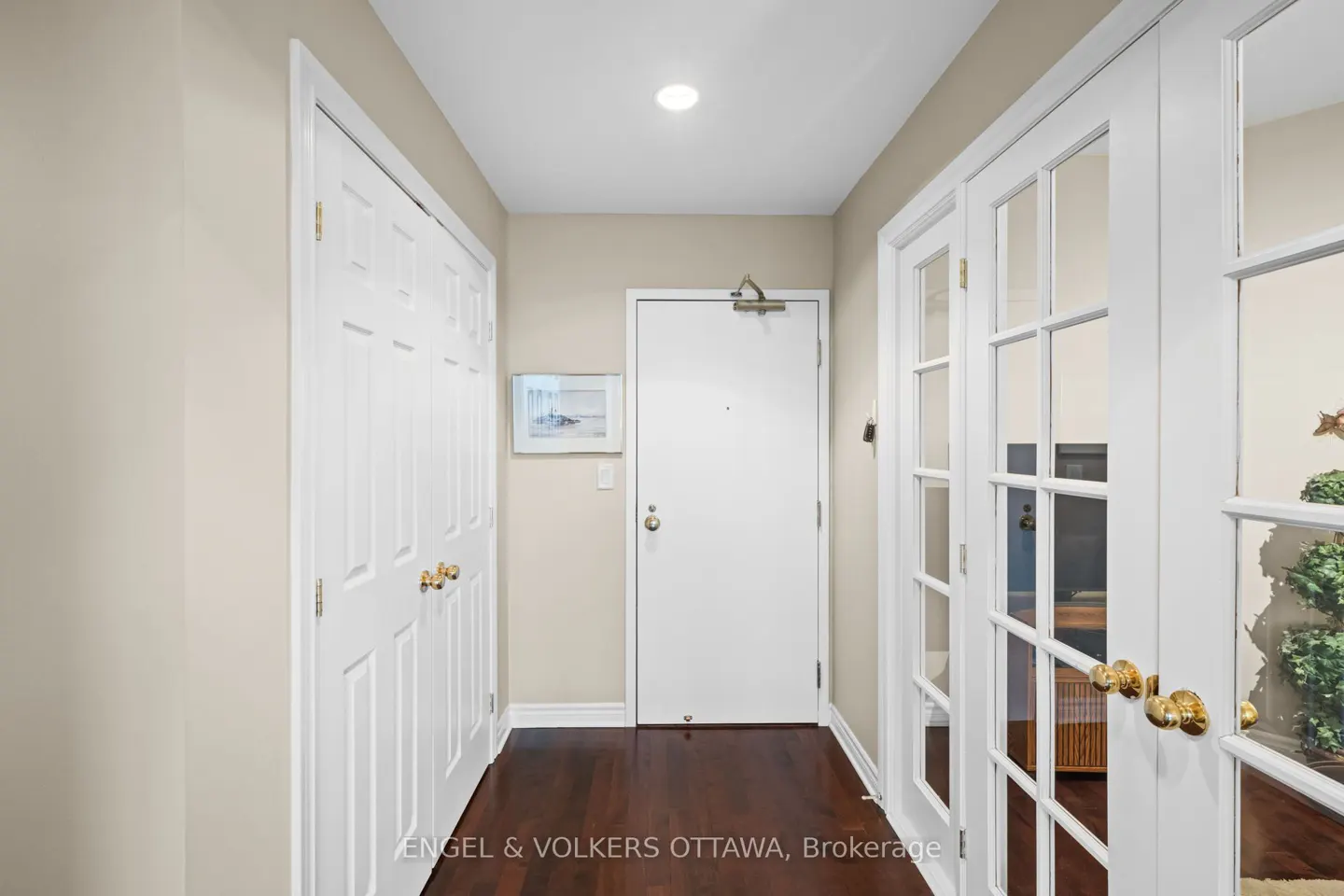 Hallway with dark wood floors, beige walls, and white doors. A closet is on the left, and glass paneled doors are on the right.
