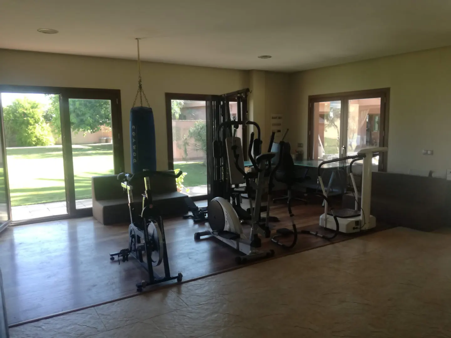 A home gym with exercise equipment, including a punching bag, stationary bike, and weight machine, with a view of the backyard.
