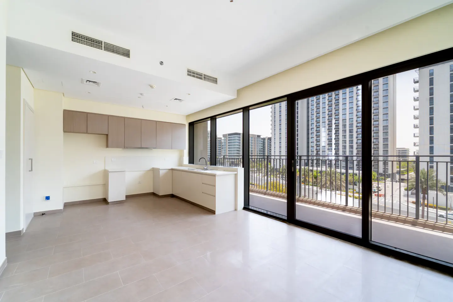 Modern kitchen with light cabinets and tile floors, featuring floor-to-ceiling windows overlooking city high-rises.