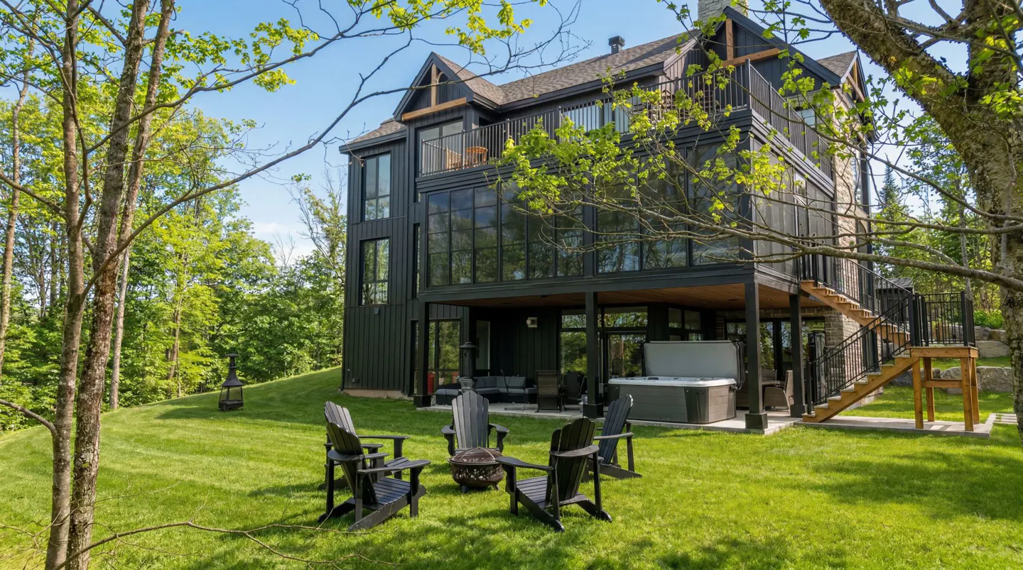 Modern black house with a deck, hot tub, and fire pit surrounded by Adirondack chairs on a green lawn.