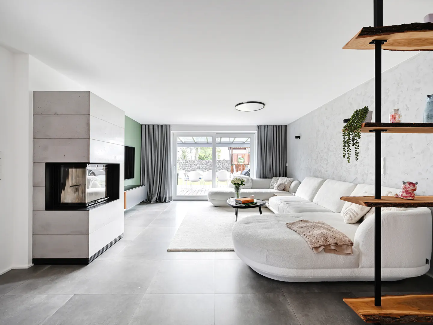 Bright living room with gray tile floors, a white sectional sofa, and a modern fireplace. Sliding glass doors lead to a backyard.